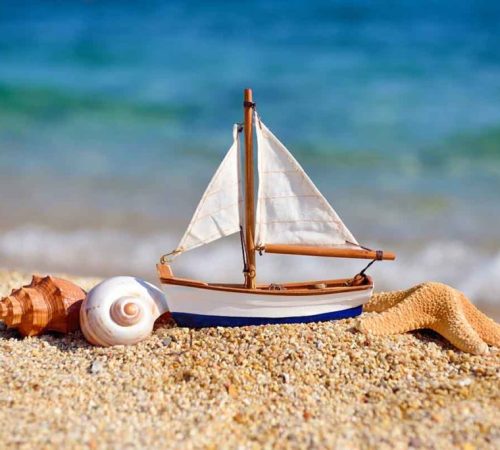 Toy ship and seashells on sand near sea. Summer vacation concept